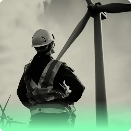 renewable a person looks at a wind turbine, they are wearing safety gear and a hard hat, which links to renewables recruiters Astute People's renewable recruitment page